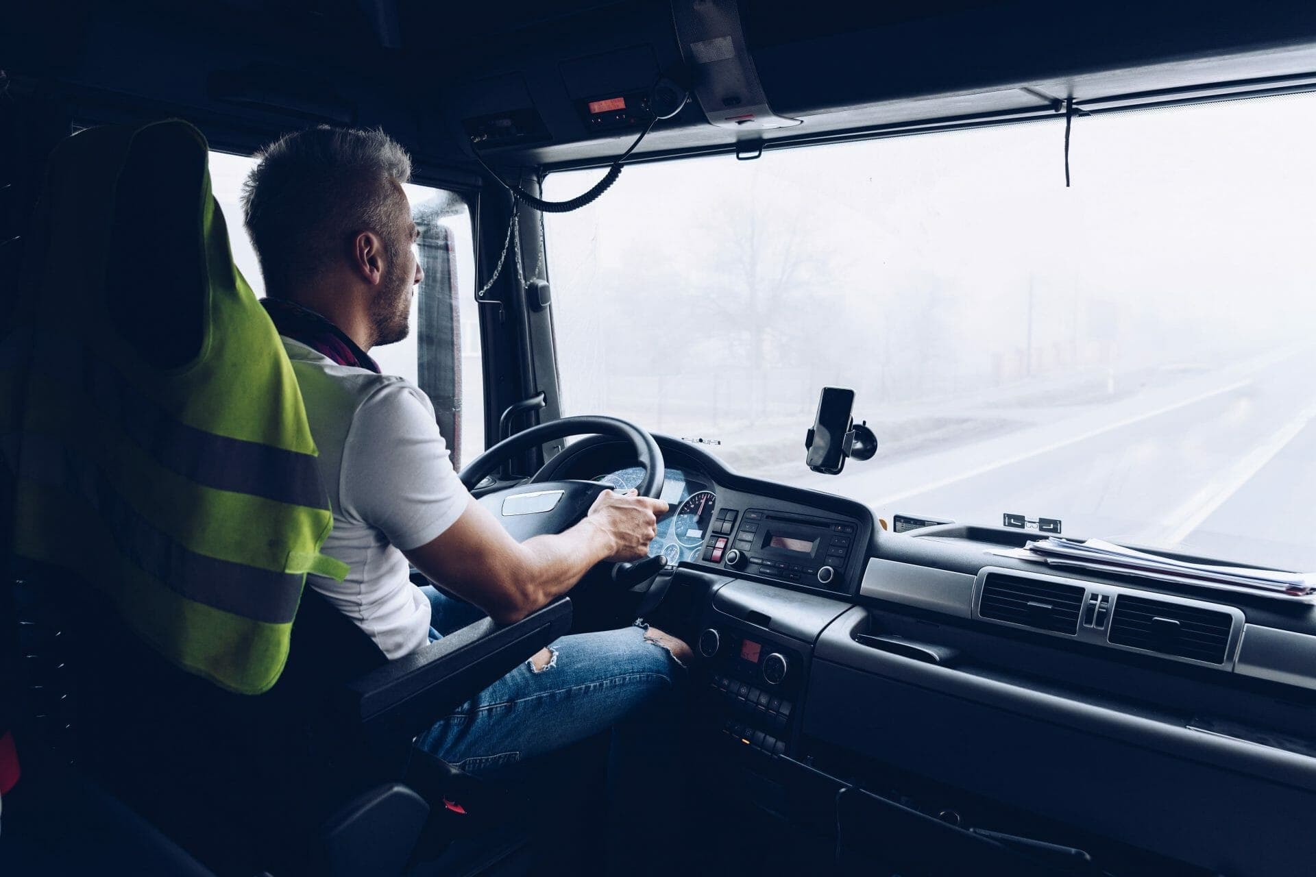 A driver in the cab of a truck, driving down a road in winter