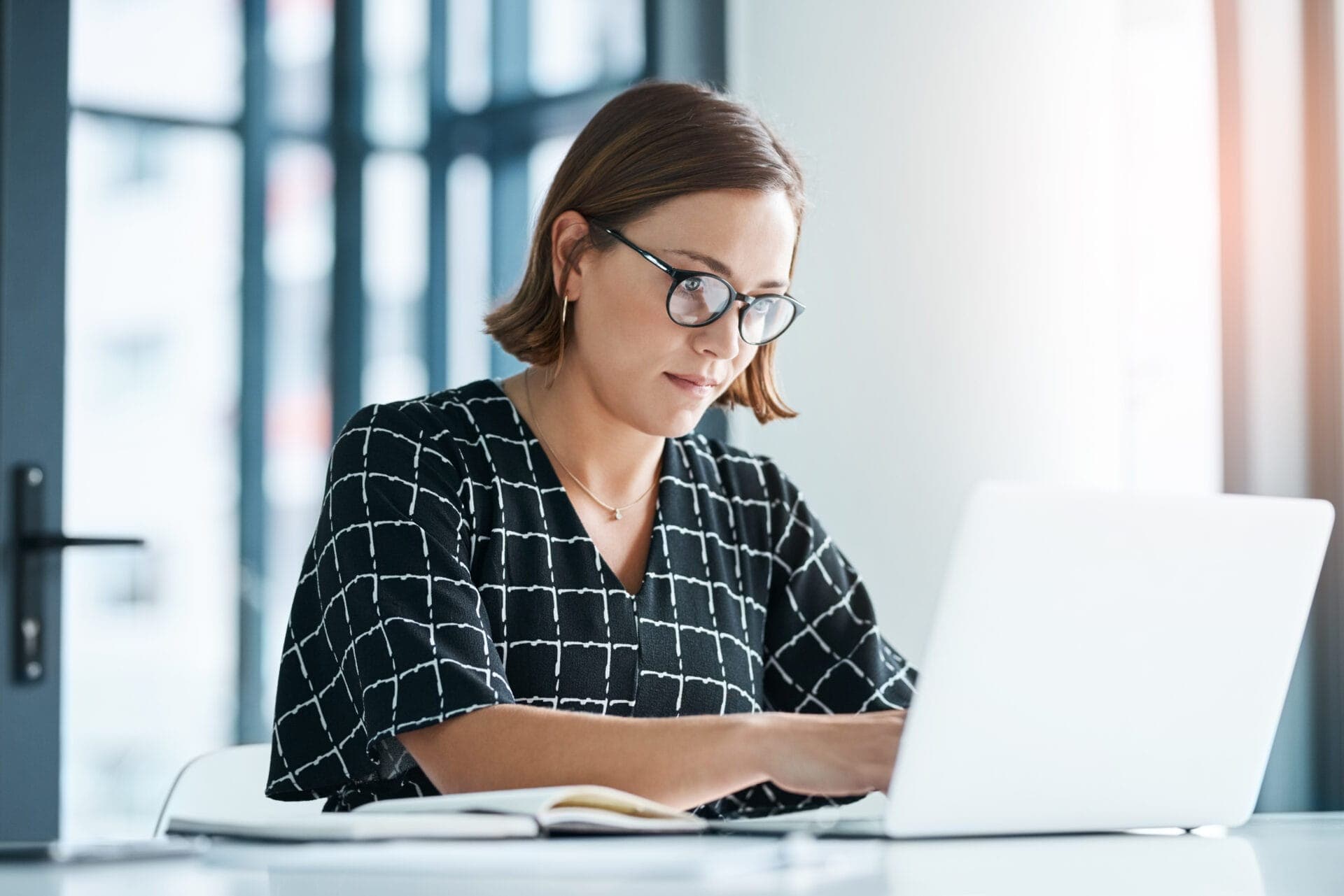 Focused researcher typing on a laptop with notes beside her, illustrating the preparation process for funding proposals in eye tracking studies.